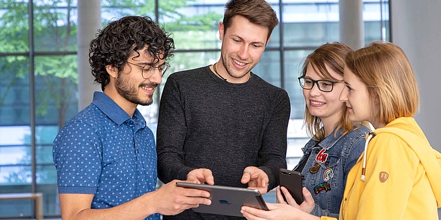 Vier Studierende schauen in ein Tablet.