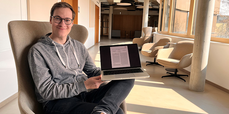 Ein Mann sitzt auf einem Sessel und hat einen Laptop am Knie.