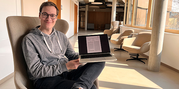 Ein Mann sitzt auf einem Sessel und hat einen Laptop am Knie.