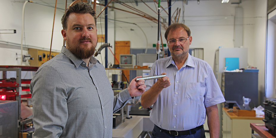 Peter Pichler und Gernot Pottlacher stehen in einem Labor und halten einen Eisenstab in der Hand.