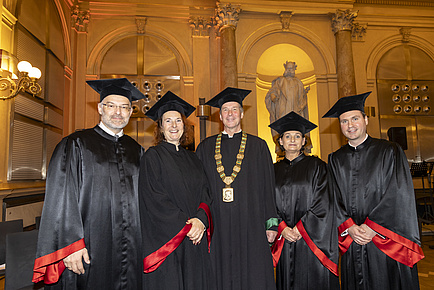 Five people dressed in robes stand next to each other and look into the camera.