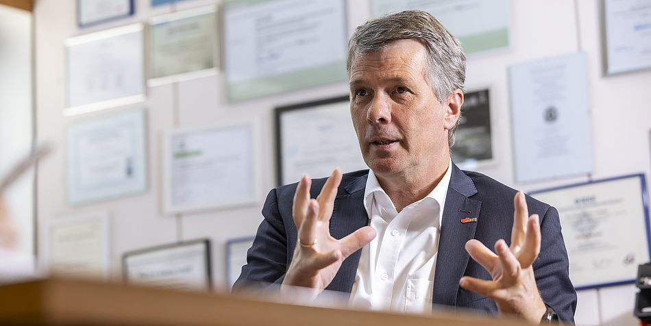 Man in white shirt and blue suit speaks straight while gesticulating. 