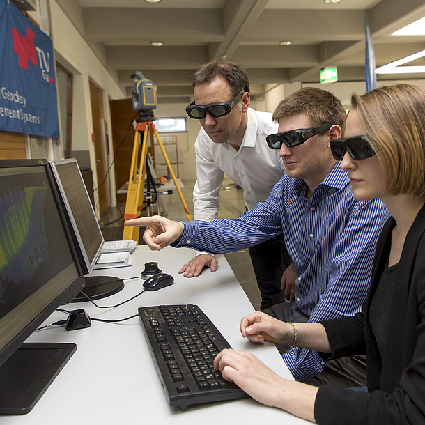 Zwei Studierende und ein Lehrender blicken durch 3D-Brillen auf eine Bildschirm mit einer Simulation.
