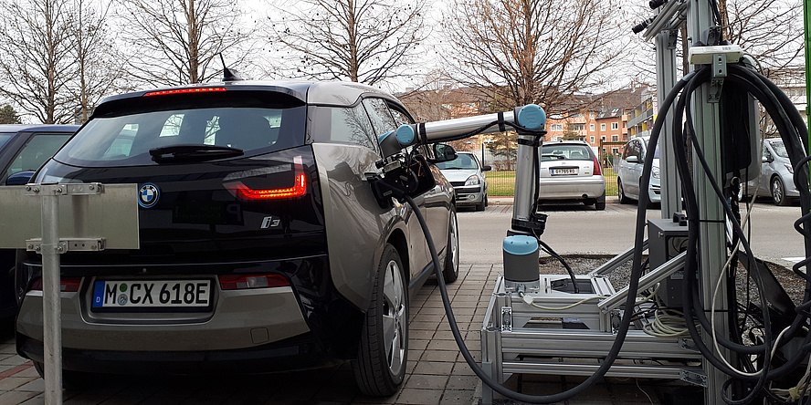 A blue electric vehicle is charged by the robot. The arm of the robot is plugged into the vehicle socket.