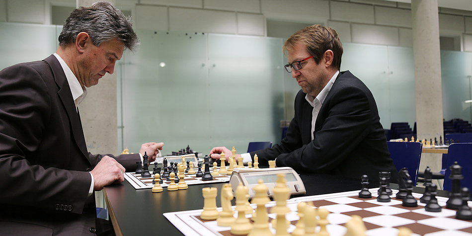 Zwei Männer sitzen an einem Tisch und spielen Schach. Beide schauen sehr konzentriert.