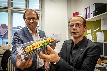 Two TU Graz researchers with a model of a tamping machine in their hands