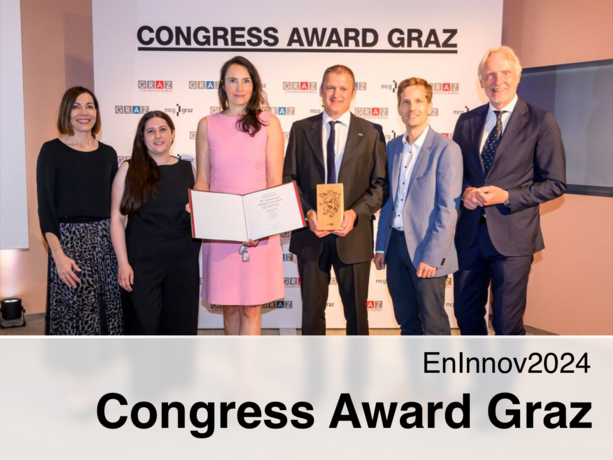 The winners are standing in front of a photo wall, holding the award in their hands.