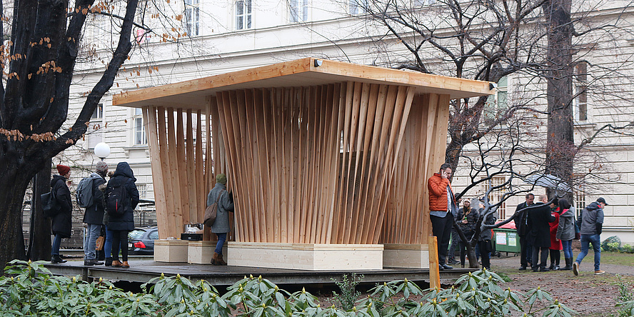 Aufnahme des Holzpavillons "Twist" mit neugierigen Besucherinnen und Besuchern im Innenhof des Campus Alte Technik.