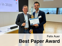 Two men in a modern conference room, one holding a microphone and the other a “Best Paper Award Certificate” with the name Felix Auer, with a presentation slide in the background reading “See you in 2028!”