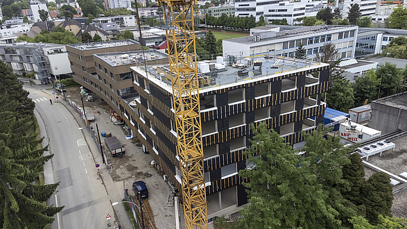 Luftaufnahme eines mehrstöckigen Gebäudes, das sich noch im Bau befindet. Im Vordergund steht ein Baukran.