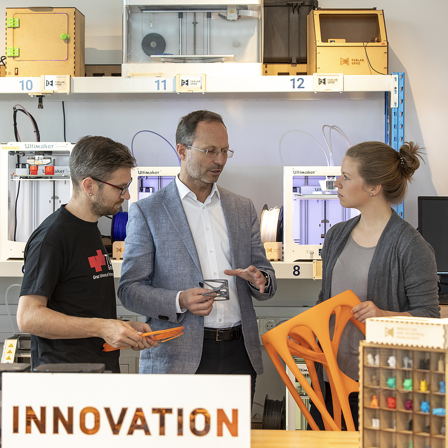 3 Personen in einem Produktions-Labor. Auf einer Box steht "Innovation".