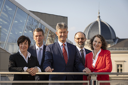 The team of two women and three men is standing in the sun - in the background the dome of a building on the campus Alte Technik.
