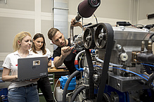 A man is screwing on a machine, two women are watching scrutinously.