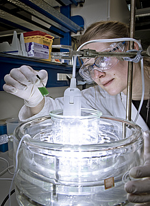 A woman in a lab coat bends over an illuminated glass container.