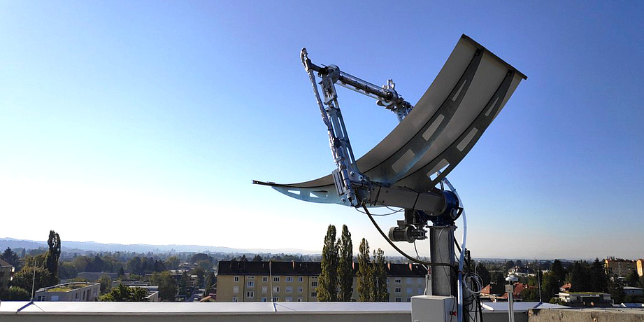 Auf dem Dach eines Bürogebäudes steht ein zur Sonne ausgerichtetes Parabolrinnen-Solarmodul.