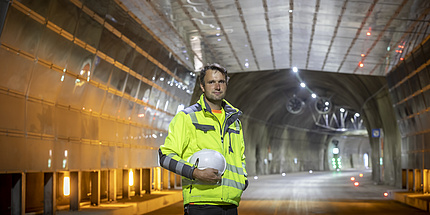Man with protective jacket and helmet under his arm stands in front of a tunnel entrance.