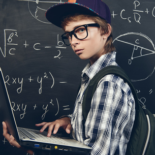 Ein Schüler mit Notebook in der Hand steht vor einer Tafel 
