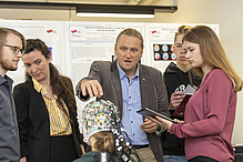 A man speaks to four students and points to a hood with many cables.