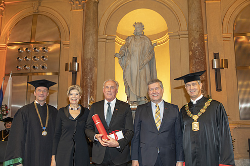 Fünf Menschen stehen vor der Statue von Kaiser Joseph II., die äußeren beiden Herren tragen einen Talar, jener in der Mitte hält eine rote Urkundenrolle in Händen. 