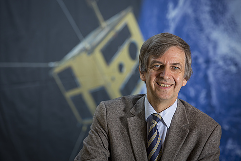 Otto Koudelka, researcher at TU Graz, in front of a photograph of the nanosatellite TUGSAT-1.