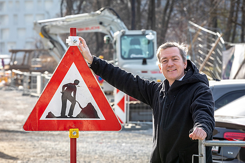 Researcher poses on a construction site next to a construction site sign