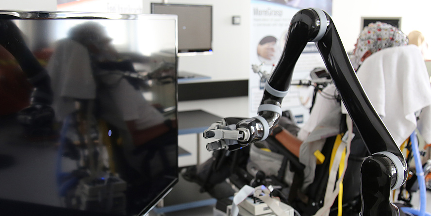 Robotic arm in front of a TV, in the background person with EEG cap