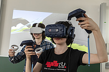 Two people are wearing VR headsets and holding controllers in their hands.