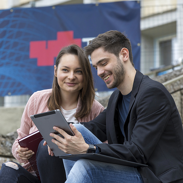 Eine junge Frau und ein junger Mann mit Tablet und Schreibblock.