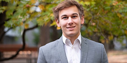 Young man with shirt and jacket in front of a tree.