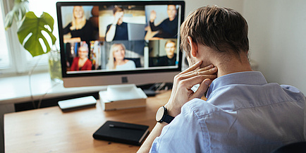 Ein Mann sitzt vor einem Bildschirm und folgt einer Videonkonferenz.