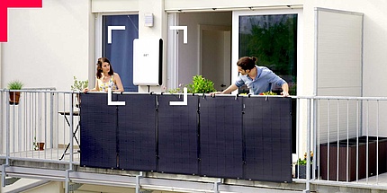 Man and woman bending over a balcony railing with solar panels.