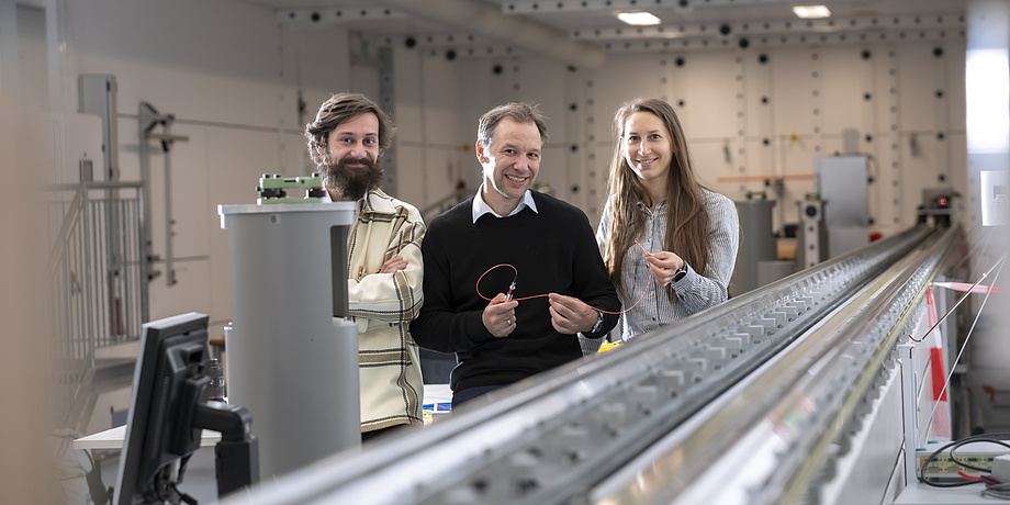 Three people holding a red glass fiber are smiling into the camera