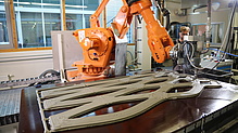 A robot arm applies a pattern of a grey substance to a flat surface.