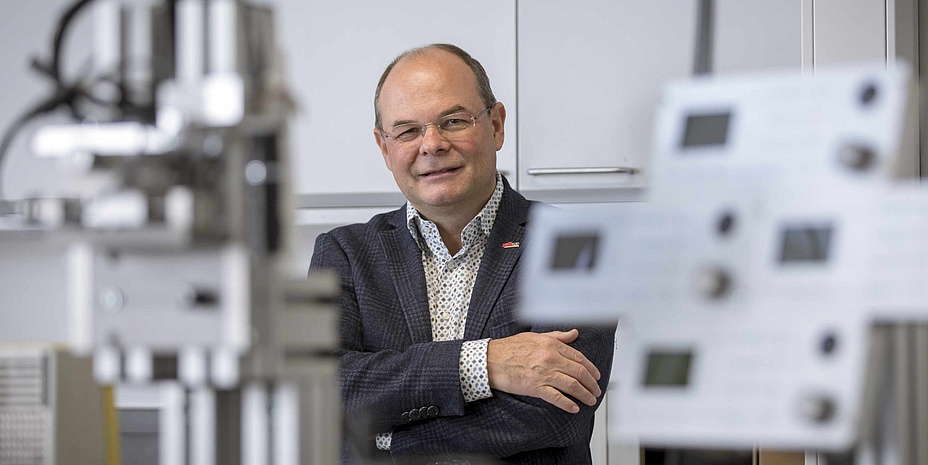 Mann mit Brille hat die Hände verschränkt und steht in einem Labor.