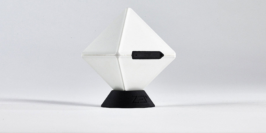 A white cube standing on a corner in a black stand. In the front is a black, elongated opening in the cube.