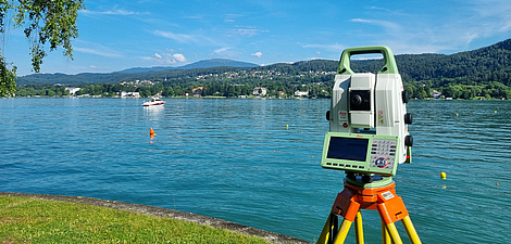 A technical device similar to a camera stands on a tripod at the shore of a lake.