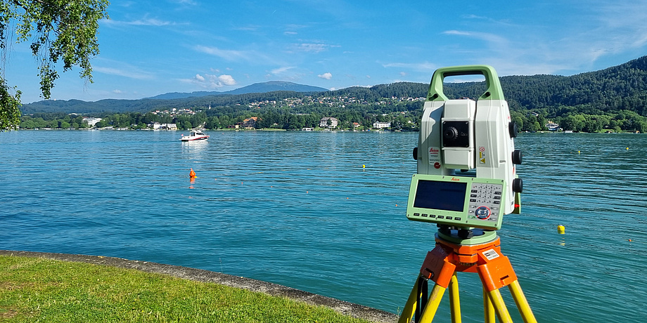 A technical device similar to a camera stands on a tripod at the shore of a lake.