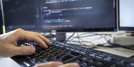 Hands on a computer keyboard, a computer screen in the background