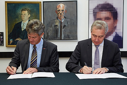 Two gentlemen in suits sitting at a table sign two contracts.