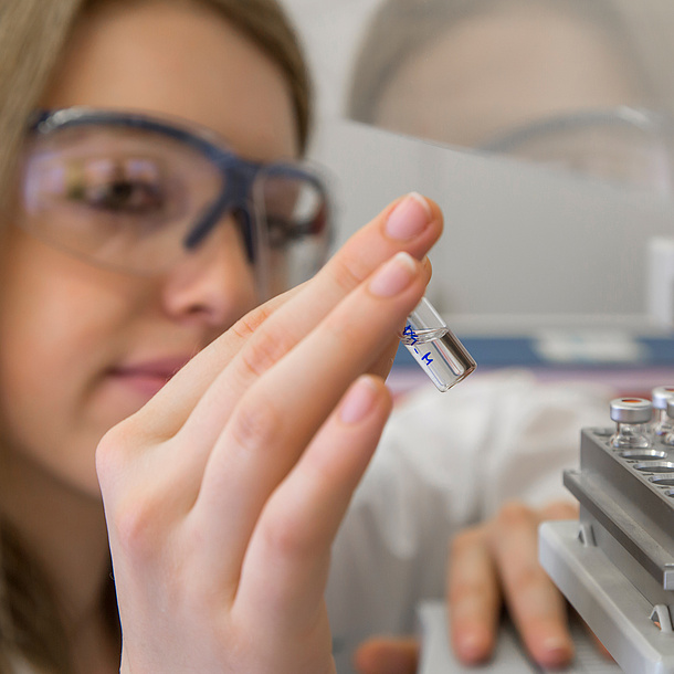 A woman wearing protective glasses is holding a tube with a laboratory sample in her hand.