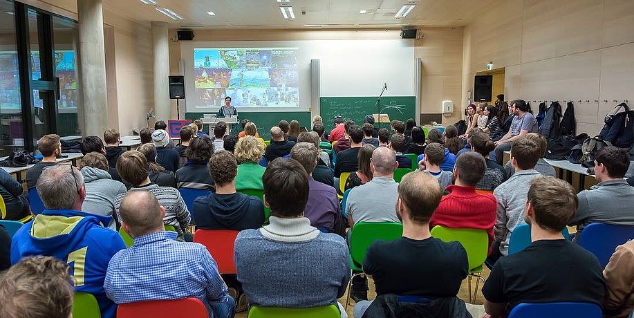 Viele Menschen sitzen in einem Hörsaal und hören einem Vortragendem zu.