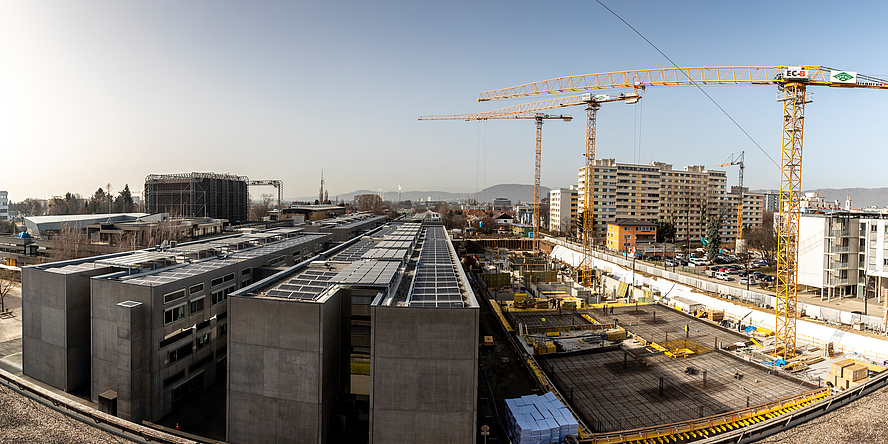 Baustellenfoto von einem Areal mit Gebäuden, Photovoltaikdächern und Kränen