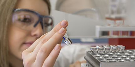 A woman in a laboratory looks scrutinizingly at a vial.
