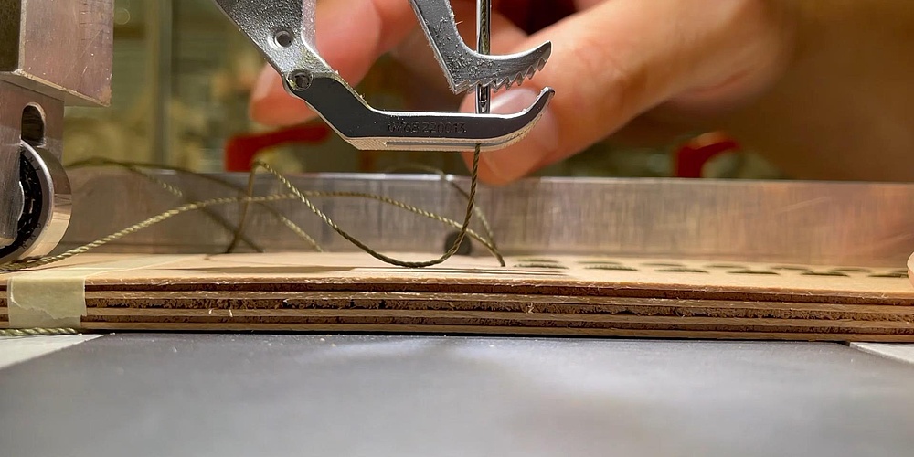 The needle of a sewing machine sews pieces of wood together using nylon thread.