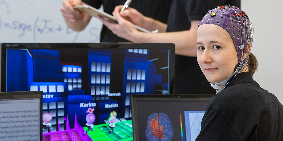 A female student of the BCI Racing Team Mirage 91 in front of a computer game, wearing a special cap to measure brain waves.