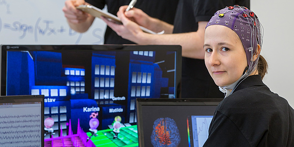 A female student of the BCI Racing Team Mirage 91 in front of a computer game, wearing a special cap to measure brain waves.