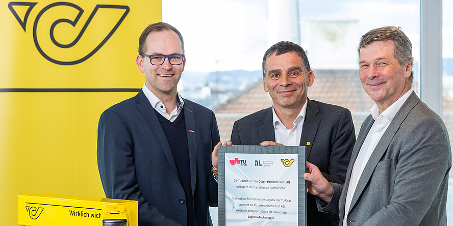 Three men smile at the camera. They are holding a plaque stating that TU Graz and Österreichische Post AG will be working together for another two years.
