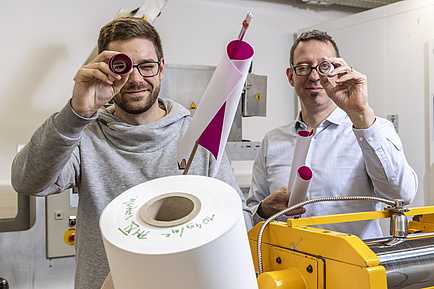 Two men look through a roll of paper.