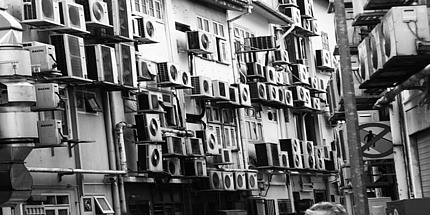Schwarz-Weiß-Foto eines Hongkonger Wohnhauses mit Klimaanlagen an der Hausfassade.