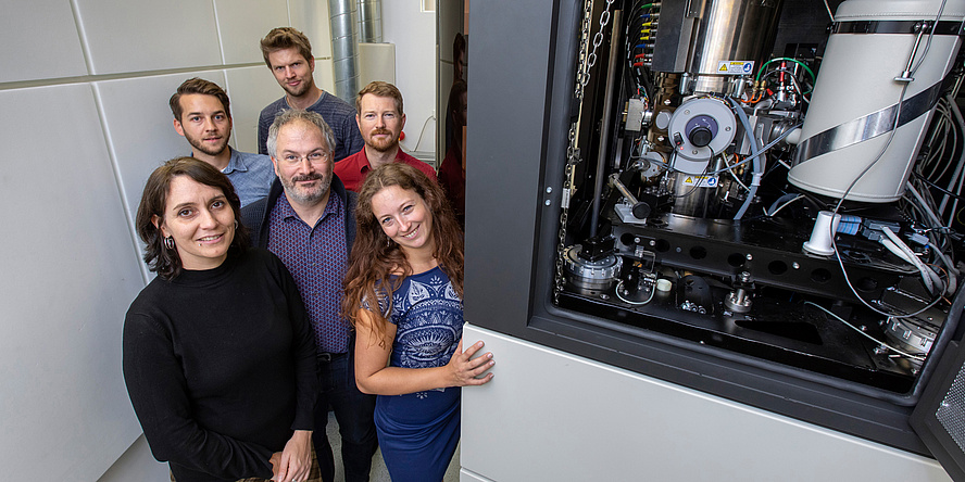 A group of researchers stands to the left of the Austrian Scanning Transmission Electron Microscope. 